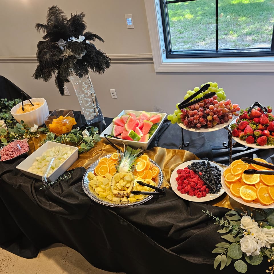 A buffet table with various fruit platters, including grapes, berries, watermelon, pineapple, and oranges.