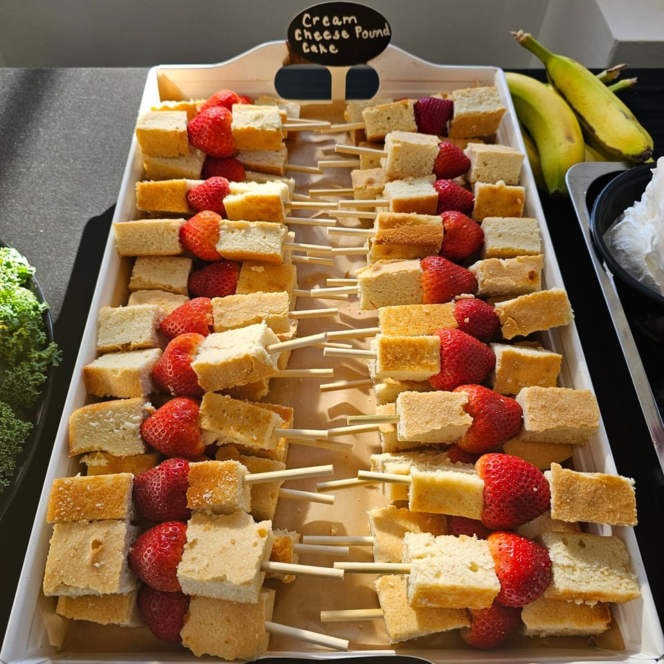 Cream cheese pound cake and strawberry skewers on a white tray, with bananas and whipped cream nearby.