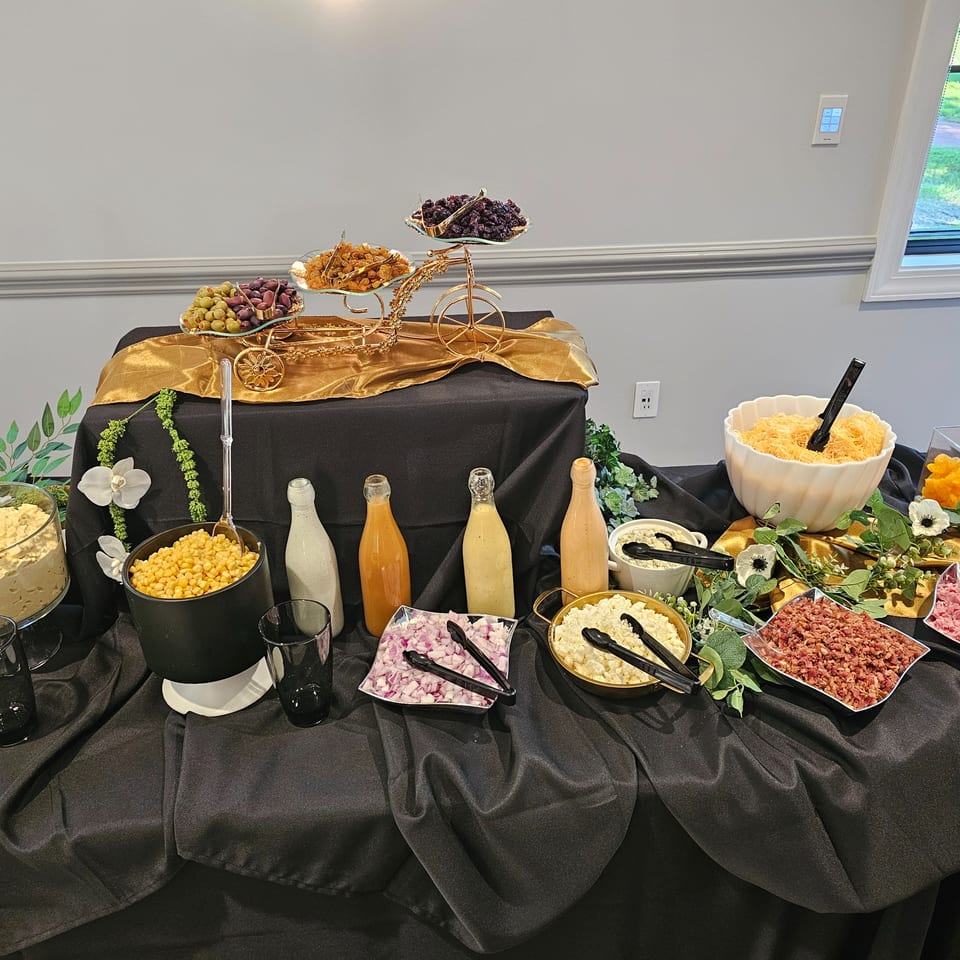 A burger topping bar with various condiments, cheeses, bacon, and vegetables on a black tablecloth.