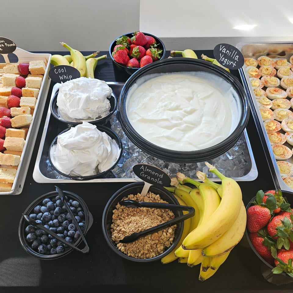 A buffet spread with vanilla yogurt, cool whip, strawberries, blueberries, bananas, granola, and deviled eggs.