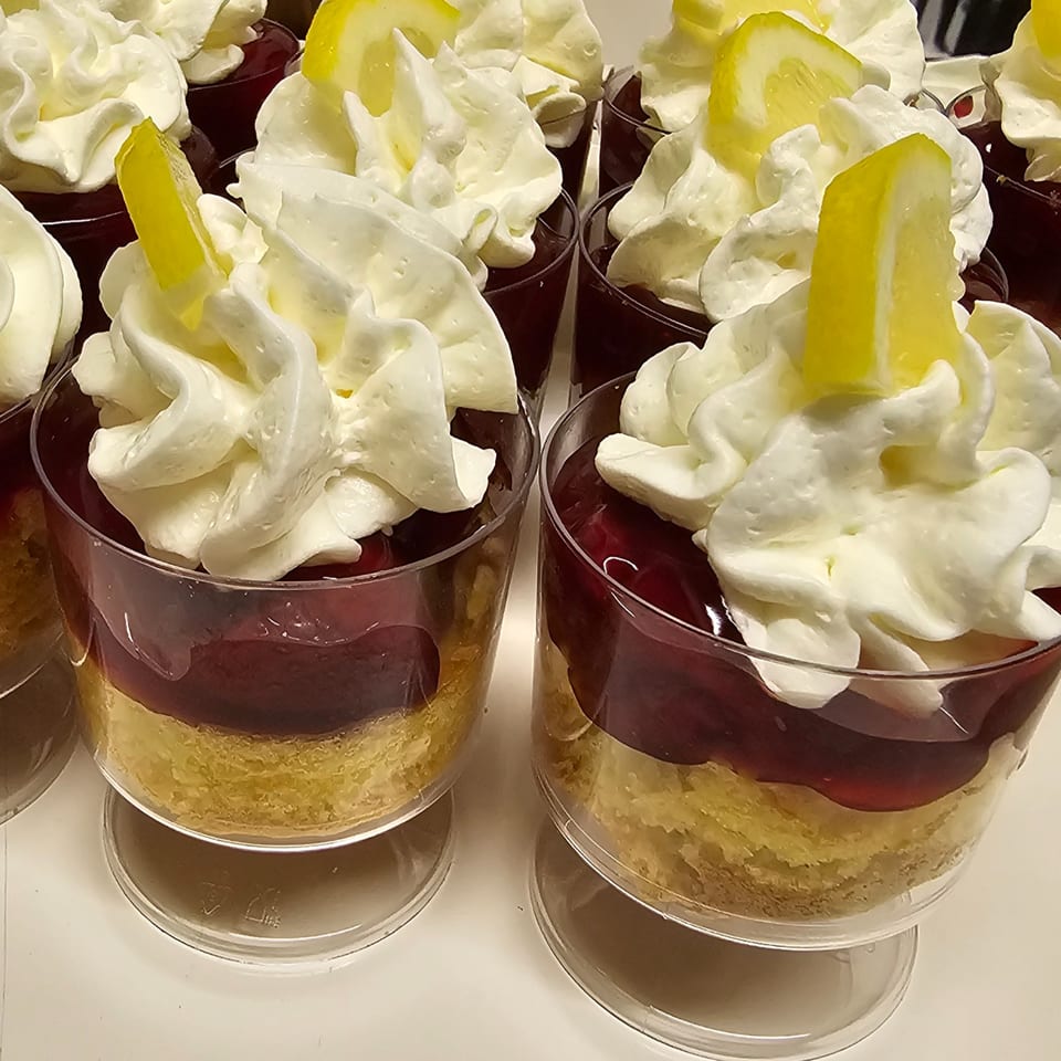 Rows of La Boca Loca NC desserts in cups with cake, red topping, whipped cream, and lemon.