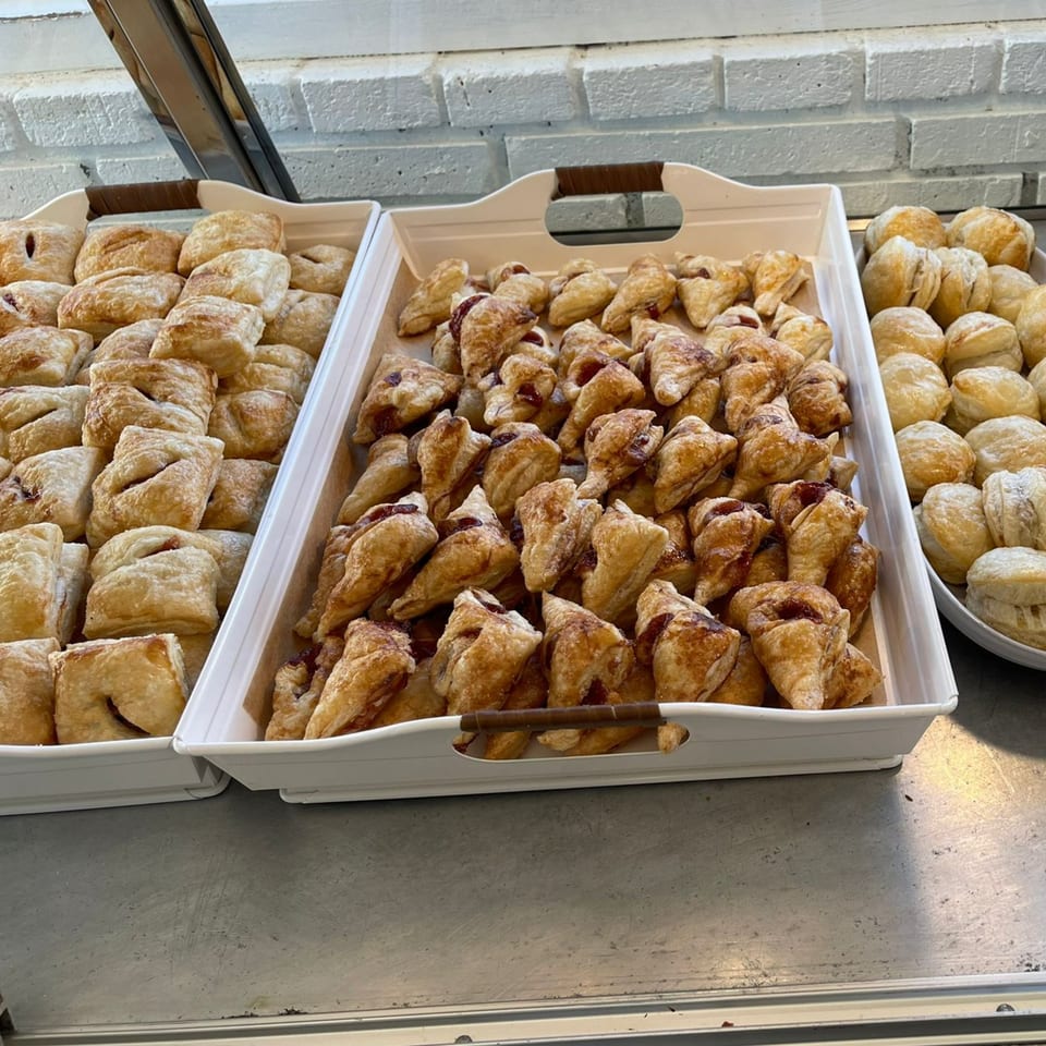 Trays of golden-brown pastries, some square with filling, others triangular, and round ones dusted with sugar.